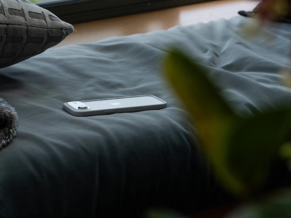 گوشی آیفون ۱۷ نقرهای روی تخت با طراحی باریک و بدنه آلومینیومی سبک